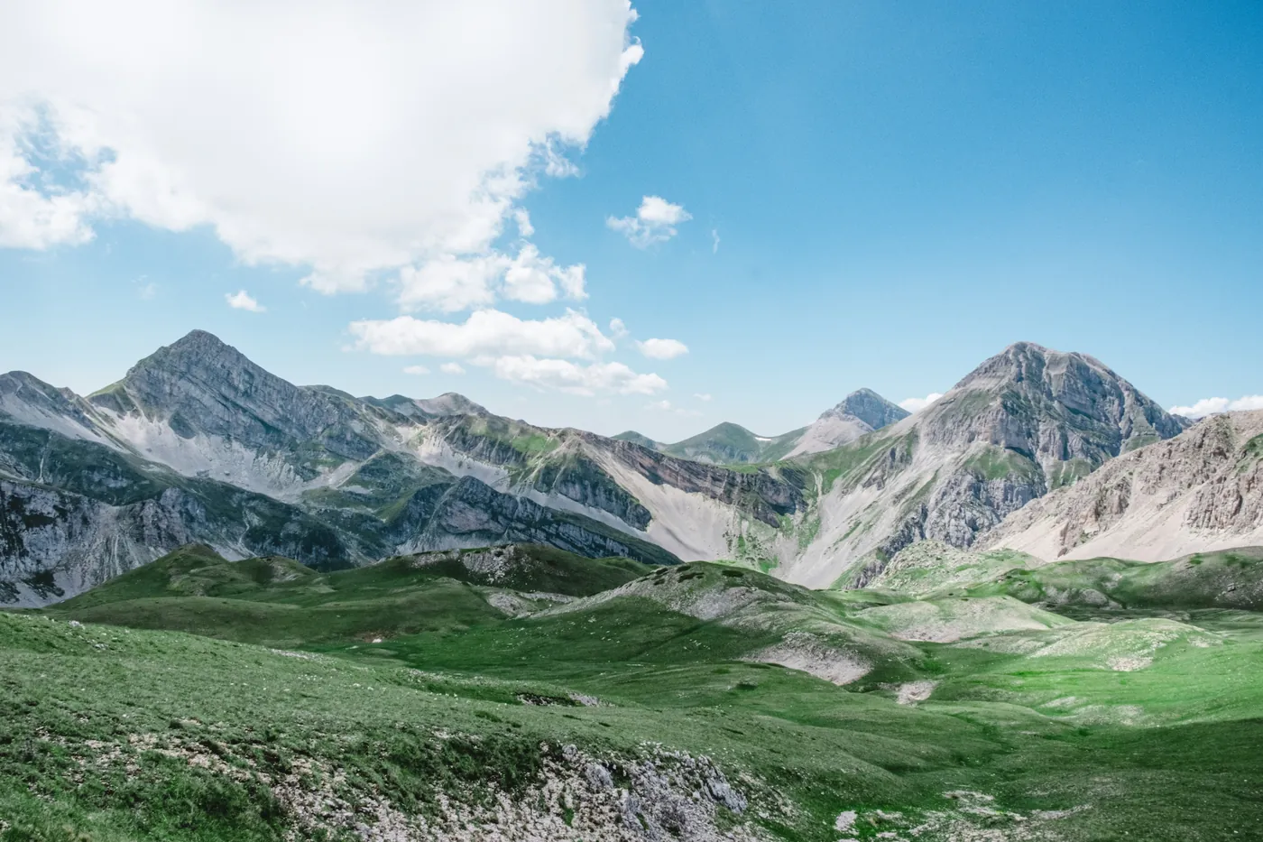 Prati verdi e crinali rocciosi dell'Appennino abruzzese sotto un cielo estivo con nuvole