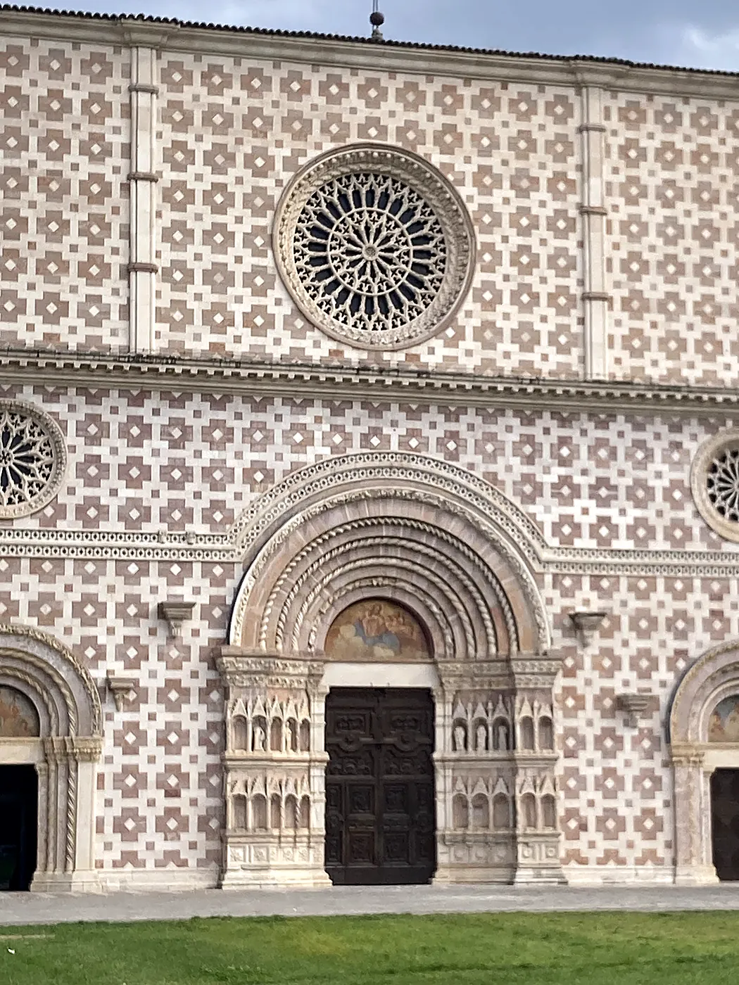 La facciata a scacchi bianchi e rosa della basilica di Santa Maria di Collemaggio all'Aquila, con il rosone e il portale.