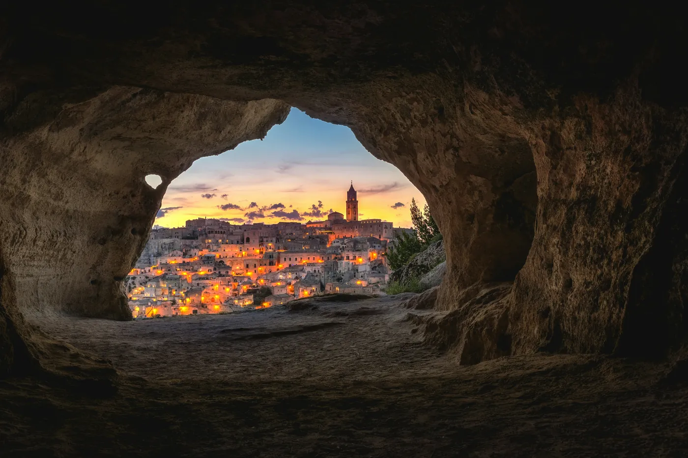 Matera al tramonto, con le luci accese, vista dall'interno di una grotta della Murgia