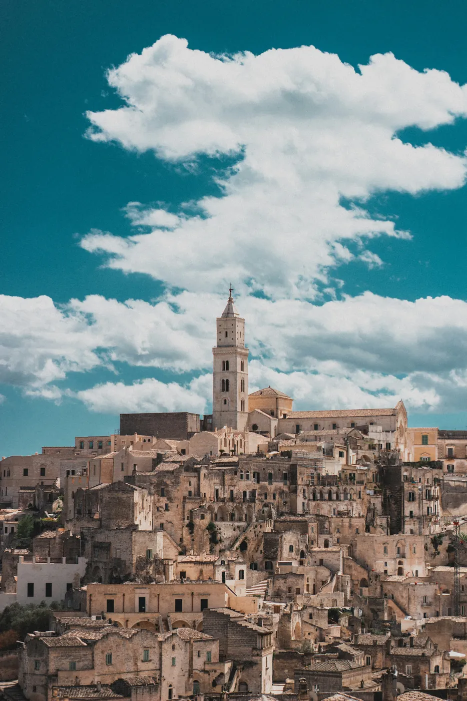 I Sassi di Matera con il campanile della cattedrale, sotto un cielo blu pieno di nuvole bianche