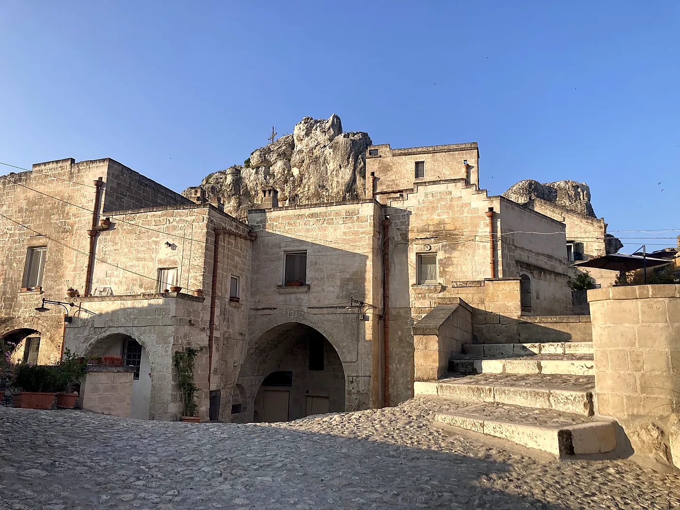 Case di tufo e scale di pietra nel Sasso Caveoso di Matera, con uno sperone di roccia alle spalle nella luce della sera.