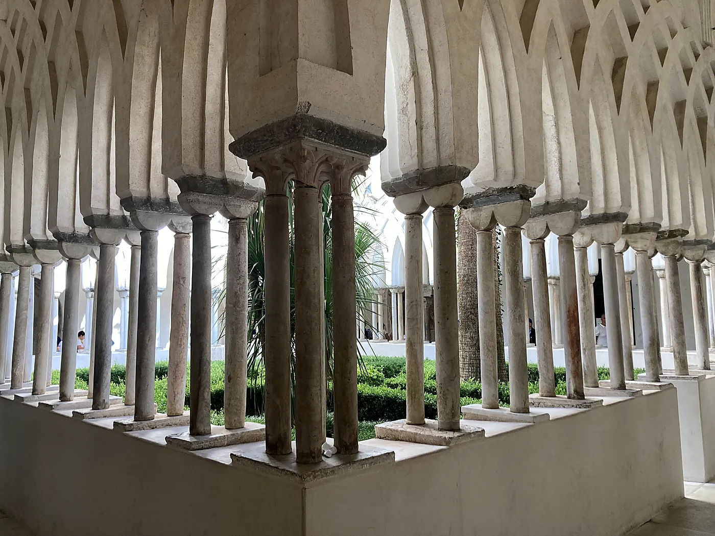 Le colonnine binate e gli archi intrecciati del Chiostro del Paradiso di Amalfi, attorno a un giardino di palme.