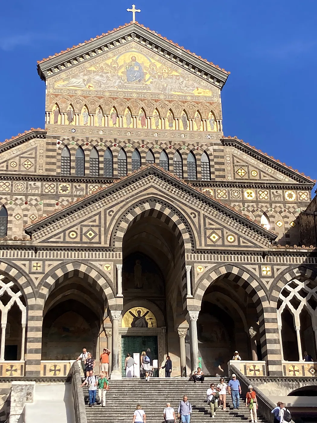 La facciata a strisce bianche e nere del Duomo di Amalfi, con il mosaico dorato del timpano e la scalinata gremita di visitatori.