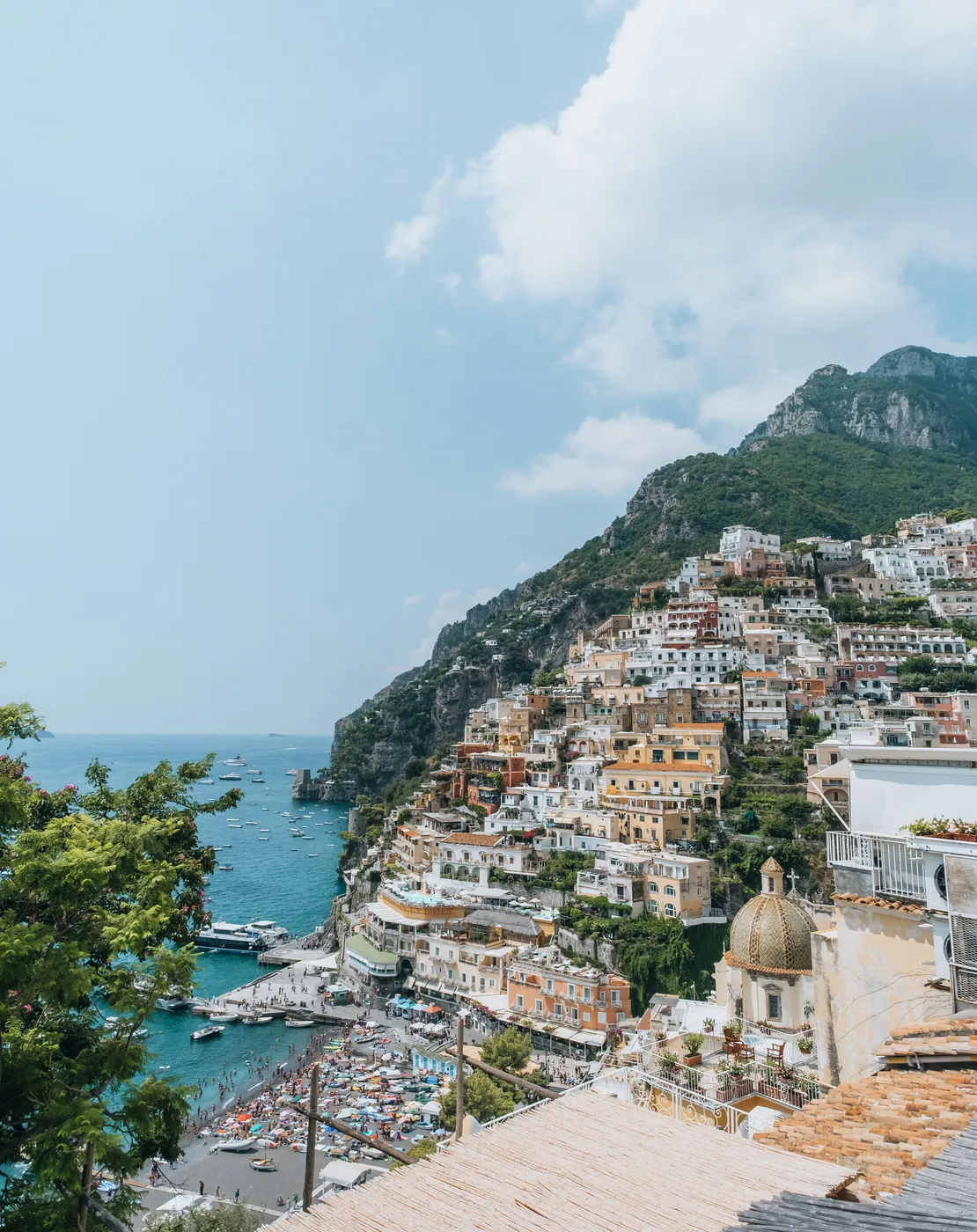 Le case colorate di Positano arrampicate sul pendio, la cupola maiolicata e la spiaggia gremita