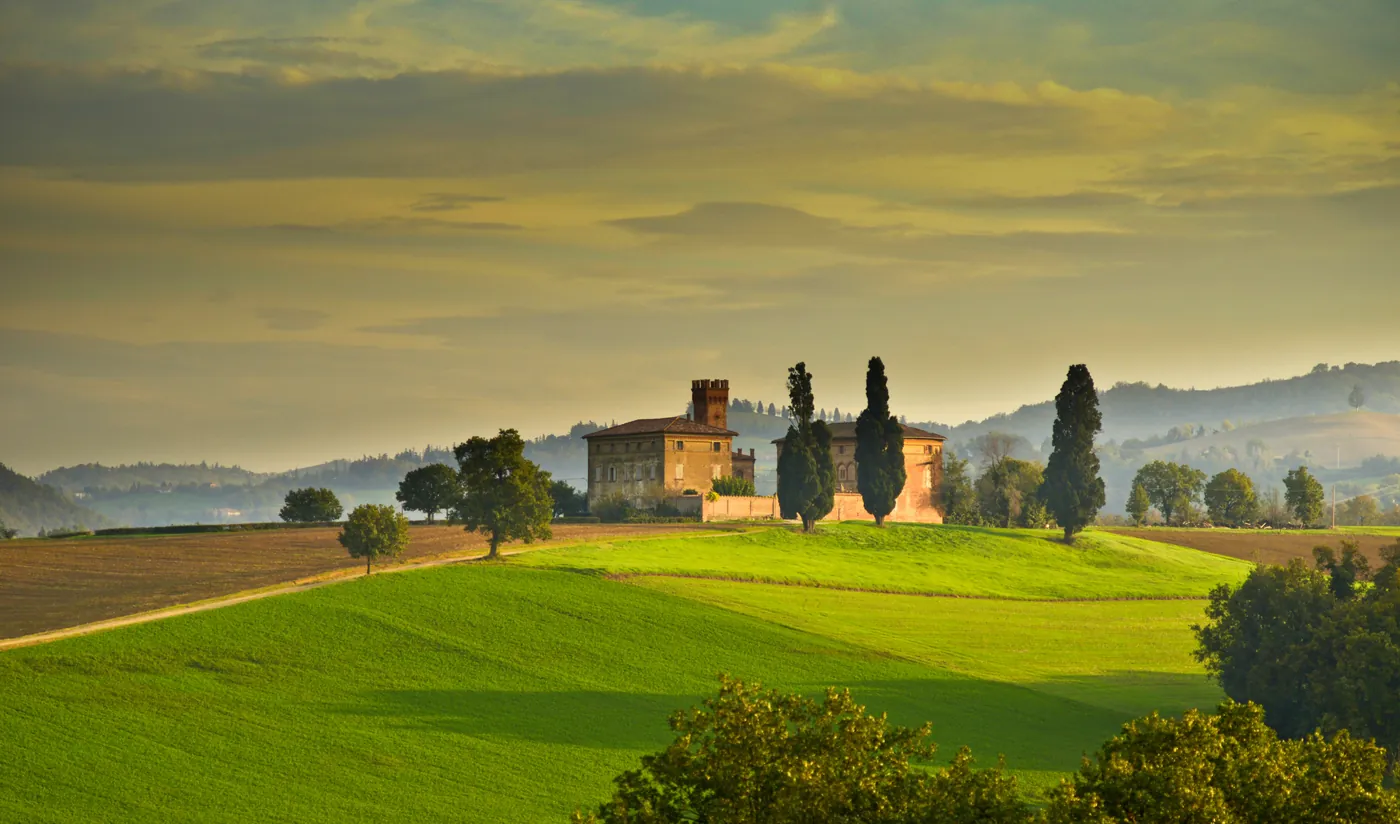 Una villa con torre tra i cipressi su una collina coltivata, al tramonto