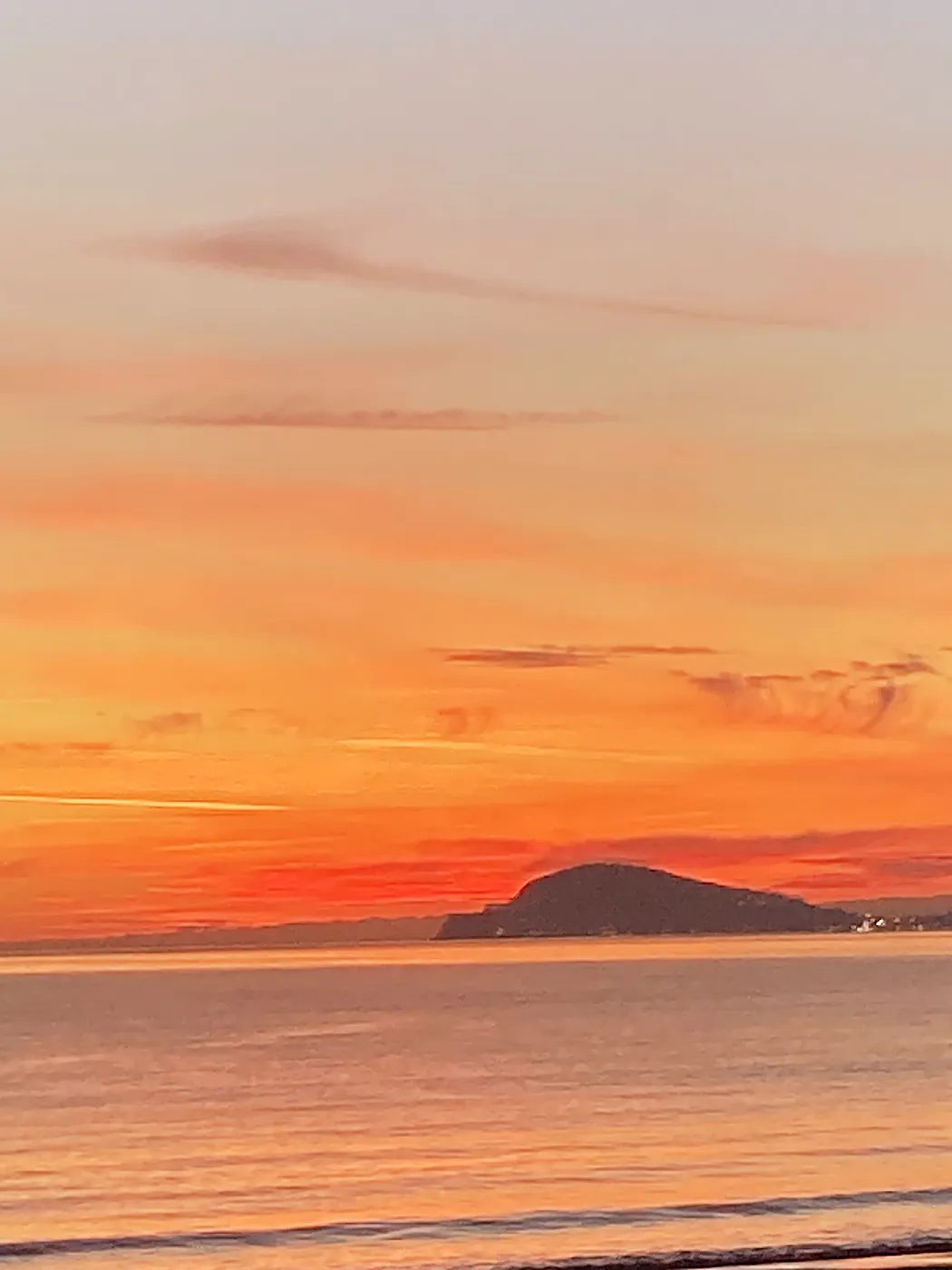 Un tramonto arancione sul mar Tirreno, con un promontorio scuro all'orizzonte e le prime luci di un paese.