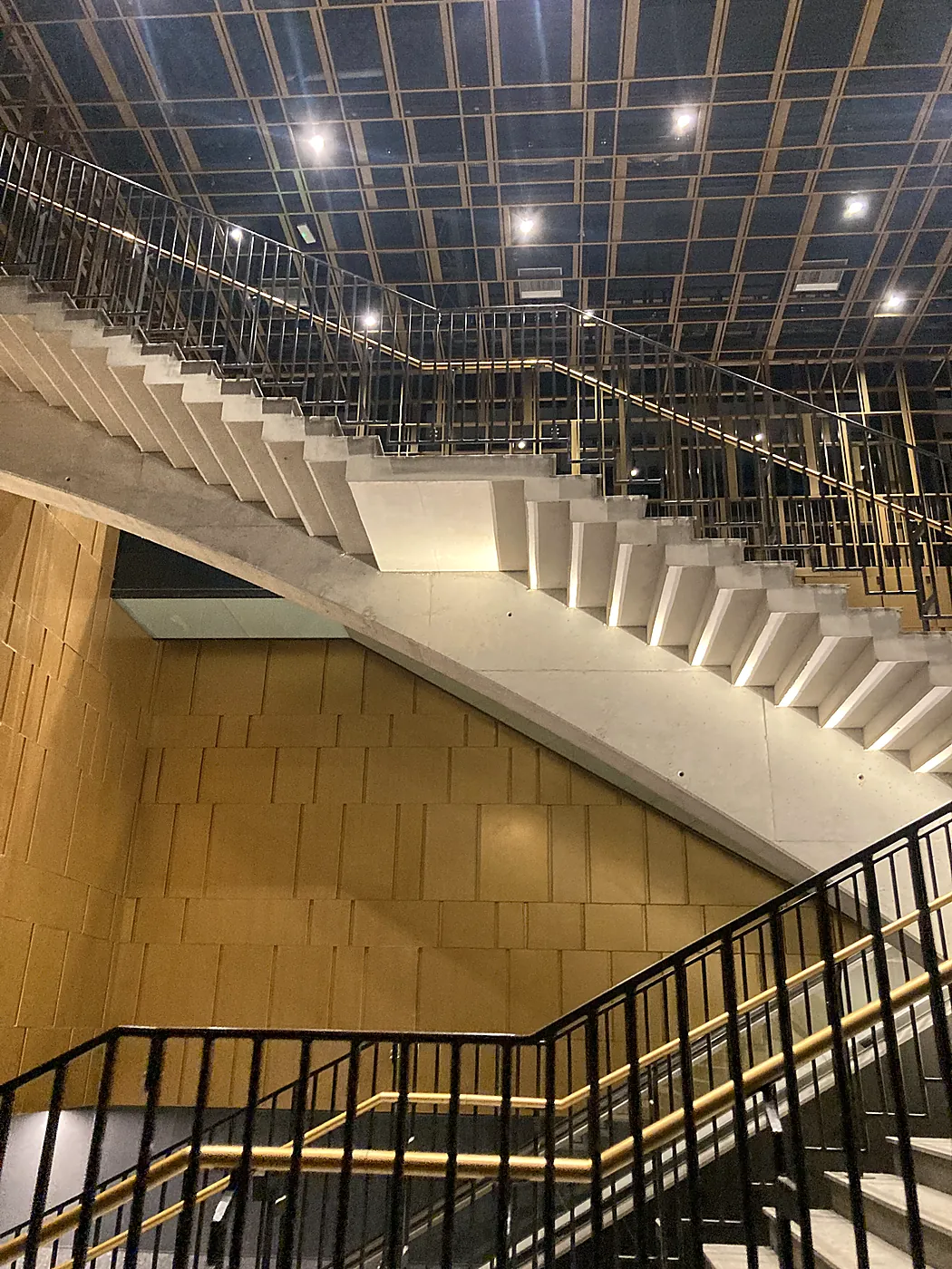 Una scala in cemento con corrimano dorati e pareti color ocra in una stazione della Metro C di Roma.