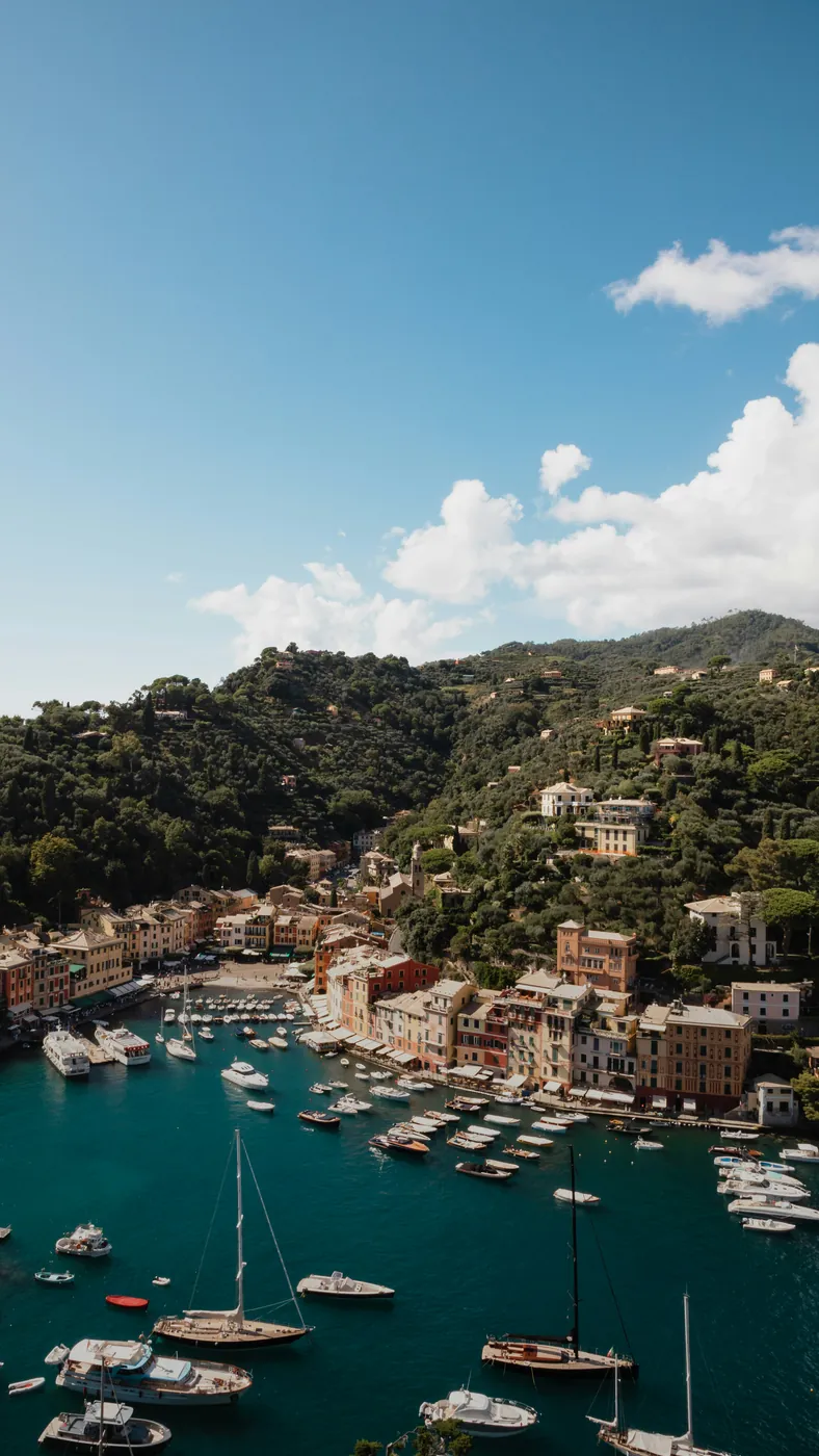 Il porticciolo di Portofino con le barche a vela e le case colorate ai piedi del promontorio verde