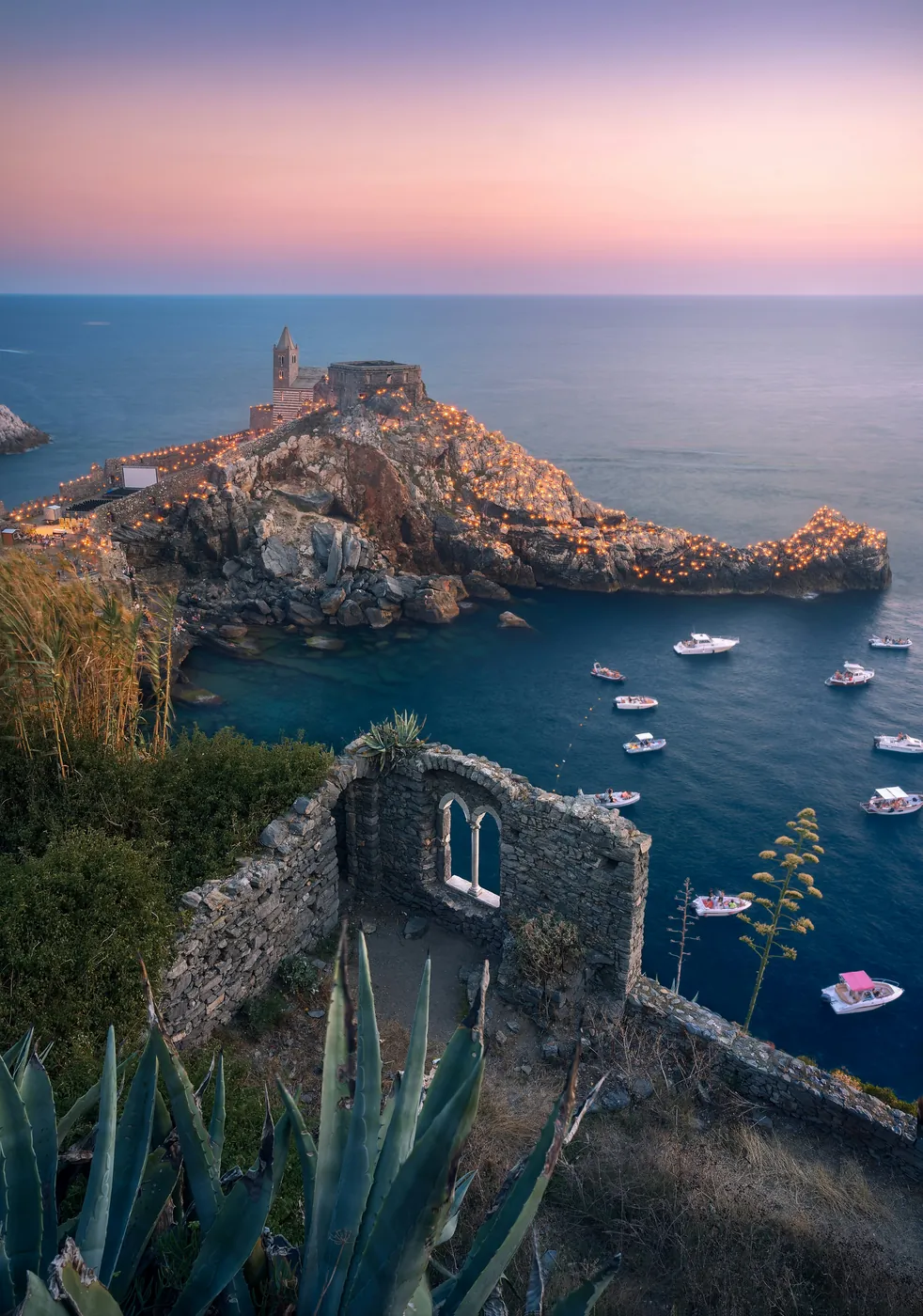 La chiesa di San Pietro sul promontorio di Portovenere, con lo scoglio illuminato dalle fiaccole al tramonto e le barche in mare