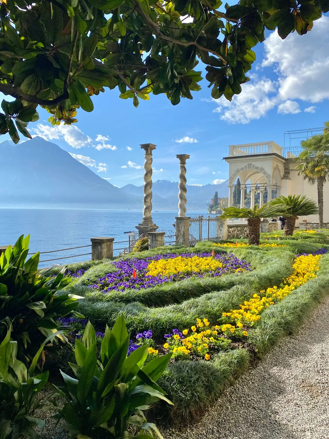 Un giardino fiorito con colonne tortili affacciato sul lago di Como e sulle montagne