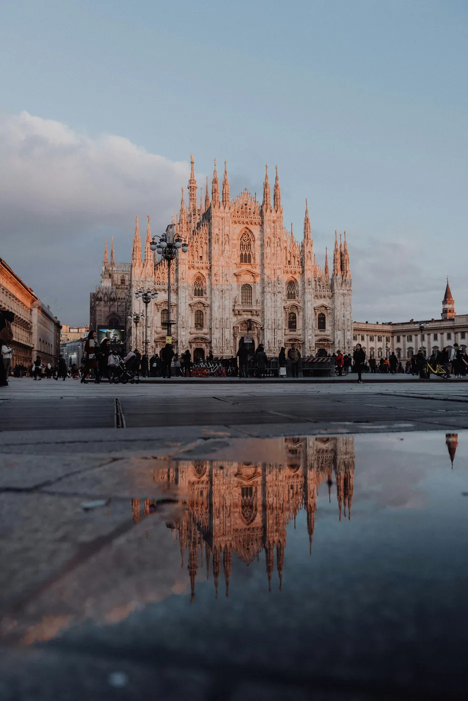La facciata del Duomo di Milano al tramonto, riflessa in una pozzanghera della piazza