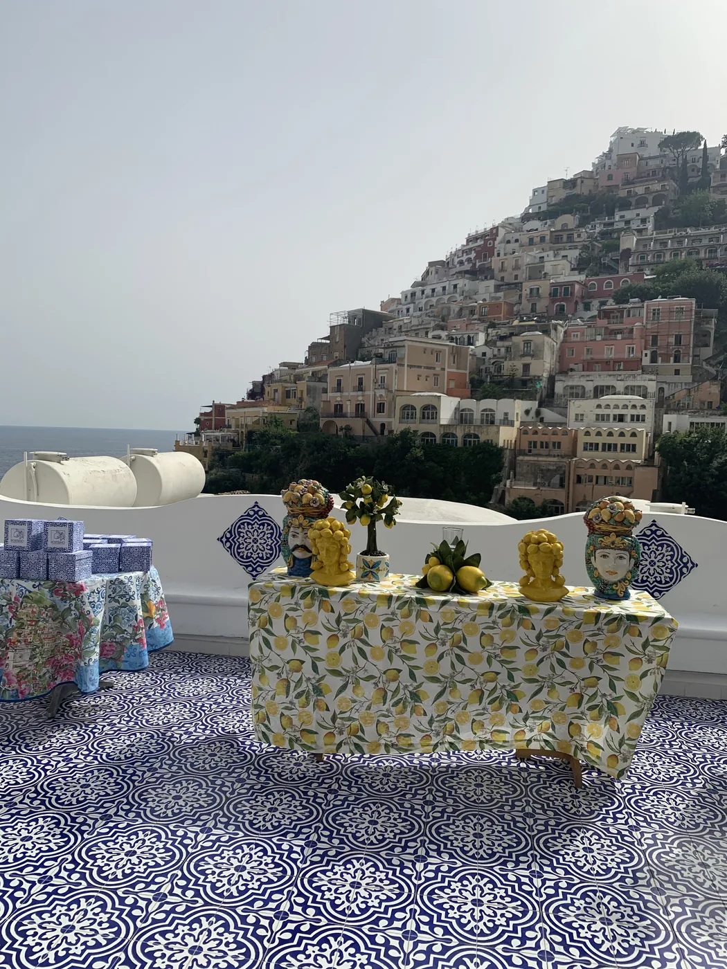 Un tavolo apparecchiato con i limoni su una terrazza di maiolica blu, il paese di Positano dietro