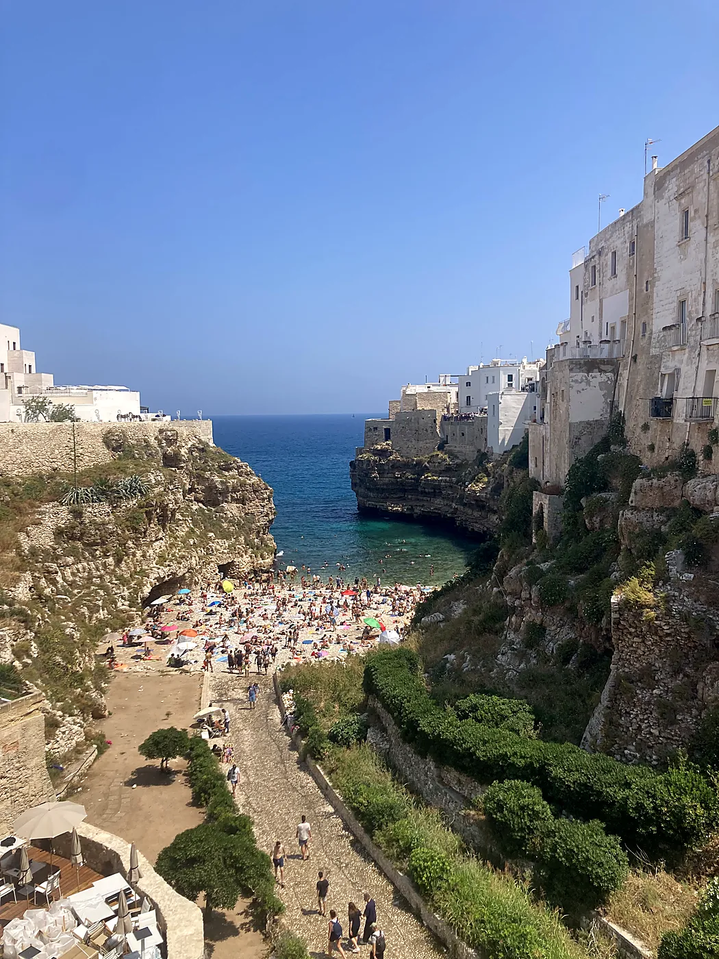 La cala di Lama Monachile a Polignano a Mare, con la spiaggia di ciottoli affollata tra le scogliere e le case bianche.