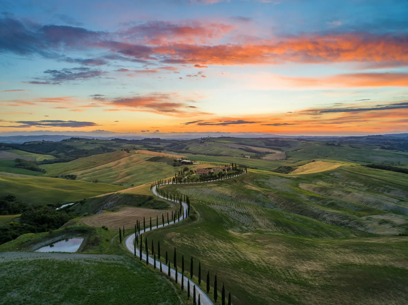 Una strada bianca fiancheggiata da cipressi che serpeggia tra le colline delle Crete Senesi al tramonto