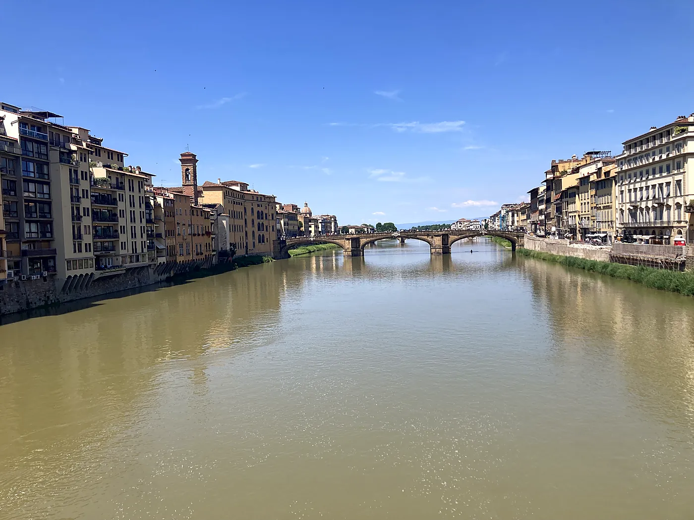 L'Arno a Firenze visto dal Ponte Vecchio, con il ponte a Santa Trinita e i palazzi dei lungarni sotto un cielo sereno.