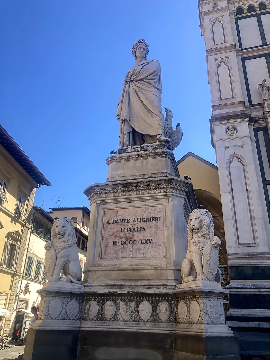 Il monumento a Dante Alighieri in piazza Santa Croce a Firenze, con i leoni di marmo alla base e la facciata della basilica sullo sfondo.