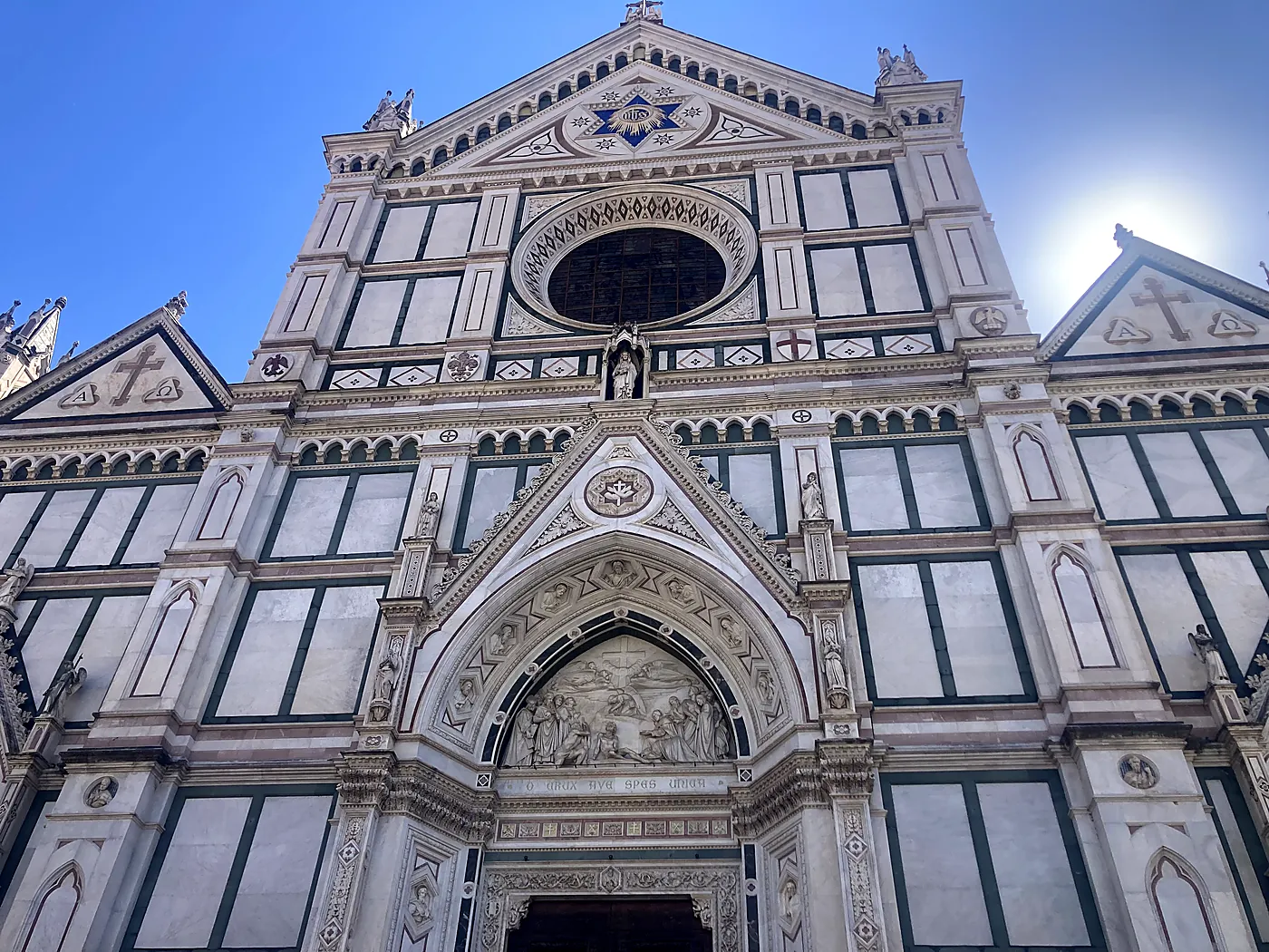 La facciata neogotica in marmi bianchi e verdi della basilica di Santa Croce a Firenze, controluce sotto il sole.