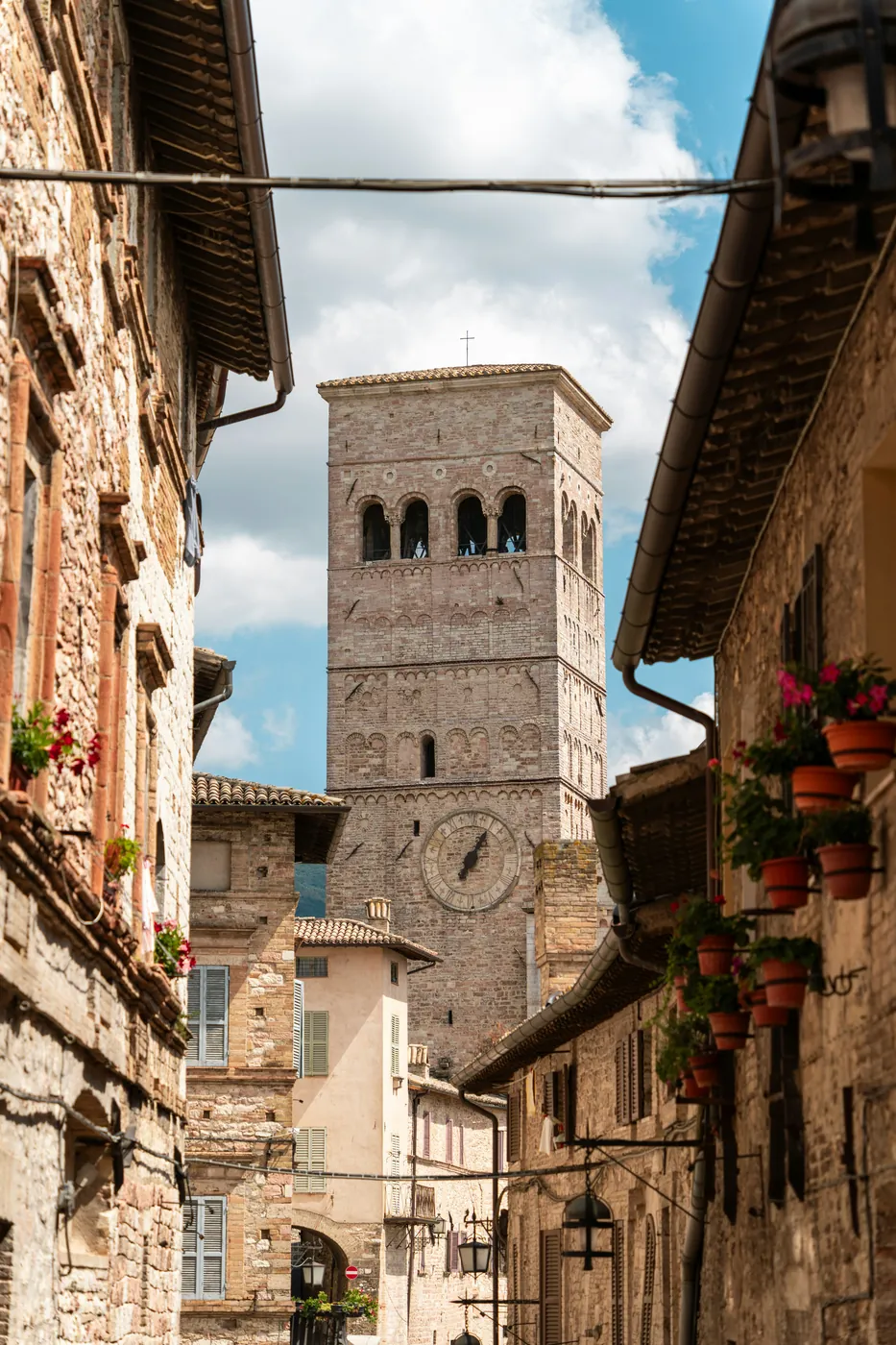 Un campanile romanico di pietra rosa con un orologio, tra le case di un borgo umbro