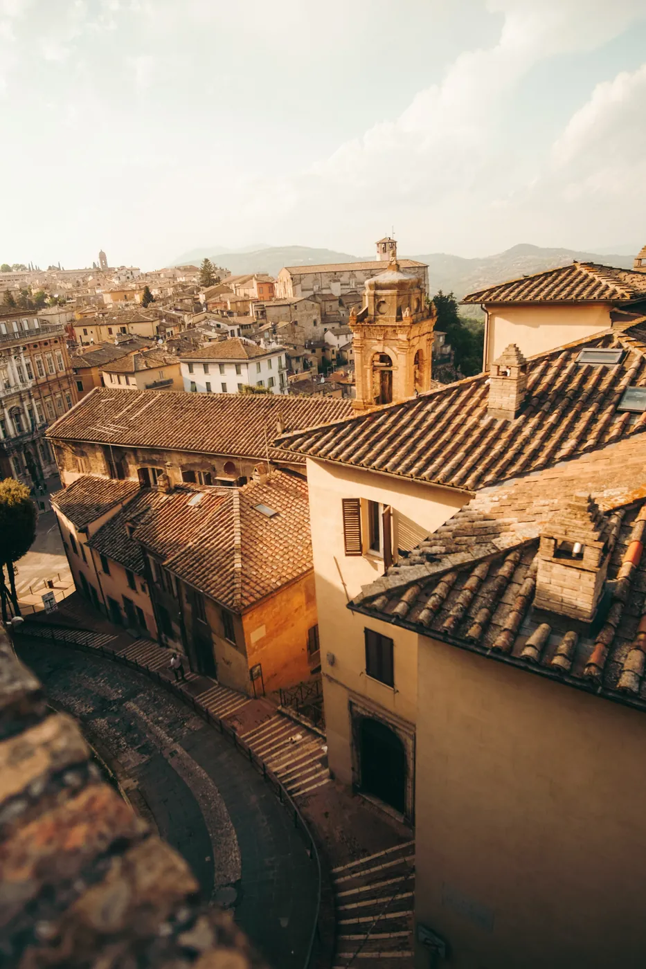 I tetti di coppi e i campanili di una città umbra sul colle, con le colline sullo sfondo