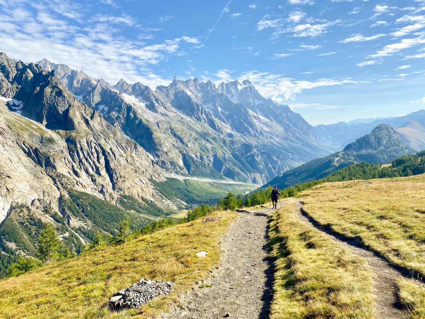 Un sentiero tra i pascoli d'alta quota con un escursionista, sotto le guglie di roccia delle Alpi