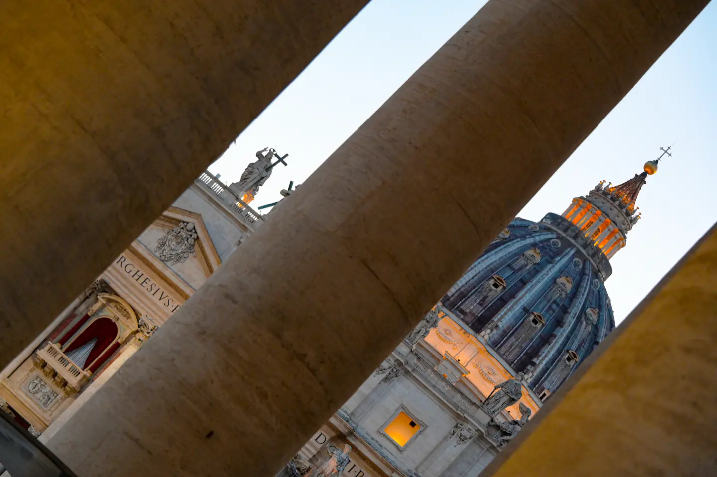 La cupola di San Pietro intravista fra le colonne del colonnato del Bernini, dorata dalla luce del tramonto