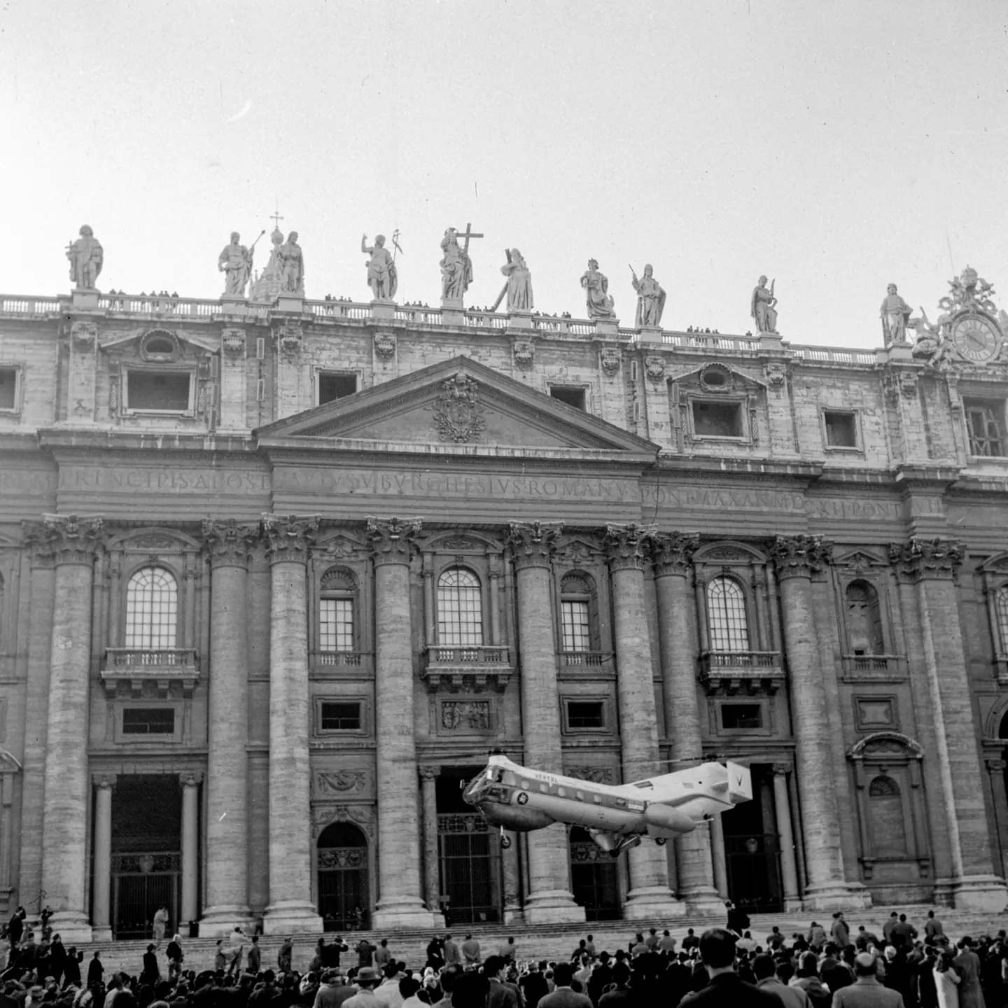 Un elicottero in volo davanti alla facciata della Basilica di San Pietro, sotto gli occhi della folla