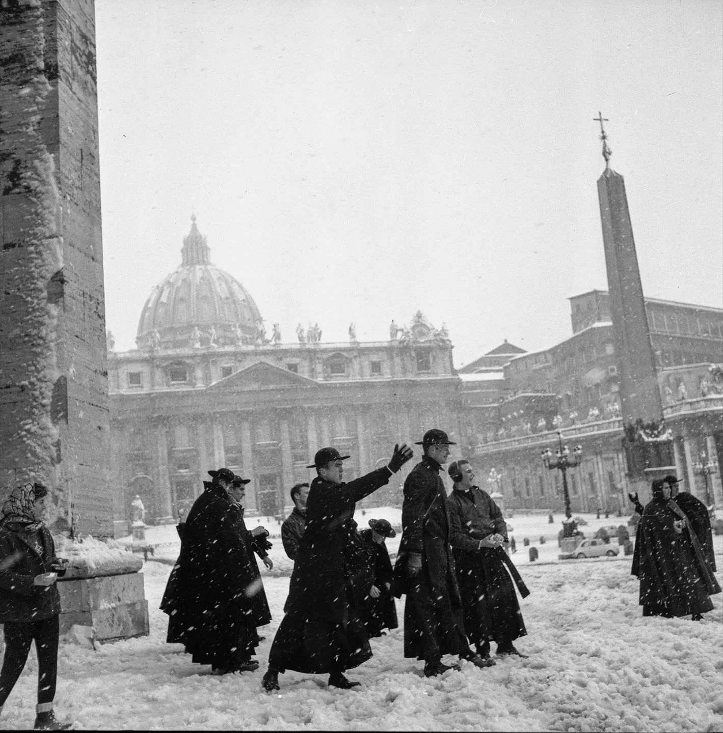 Seminaristi in mantello nero attraversano Piazza San Pietro sotto la neve