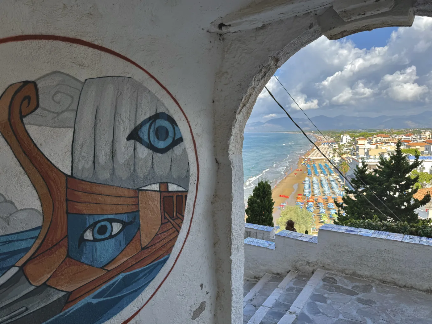 Un murale con la prua di una nave e l'occhio dipinto, sotto un arco affacciato sul mare